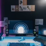 Configuração de jogos para PC com monitor, portátil, teclado e iluminação azul e rosa.