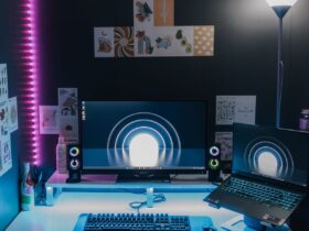 Configuração de jogos para PC com monitor, portátil, teclado e iluminação azul e rosa.