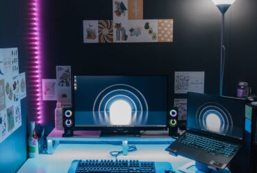 Configuração de jogos para PC com monitor, portátil, teclado e iluminação azul e rosa.