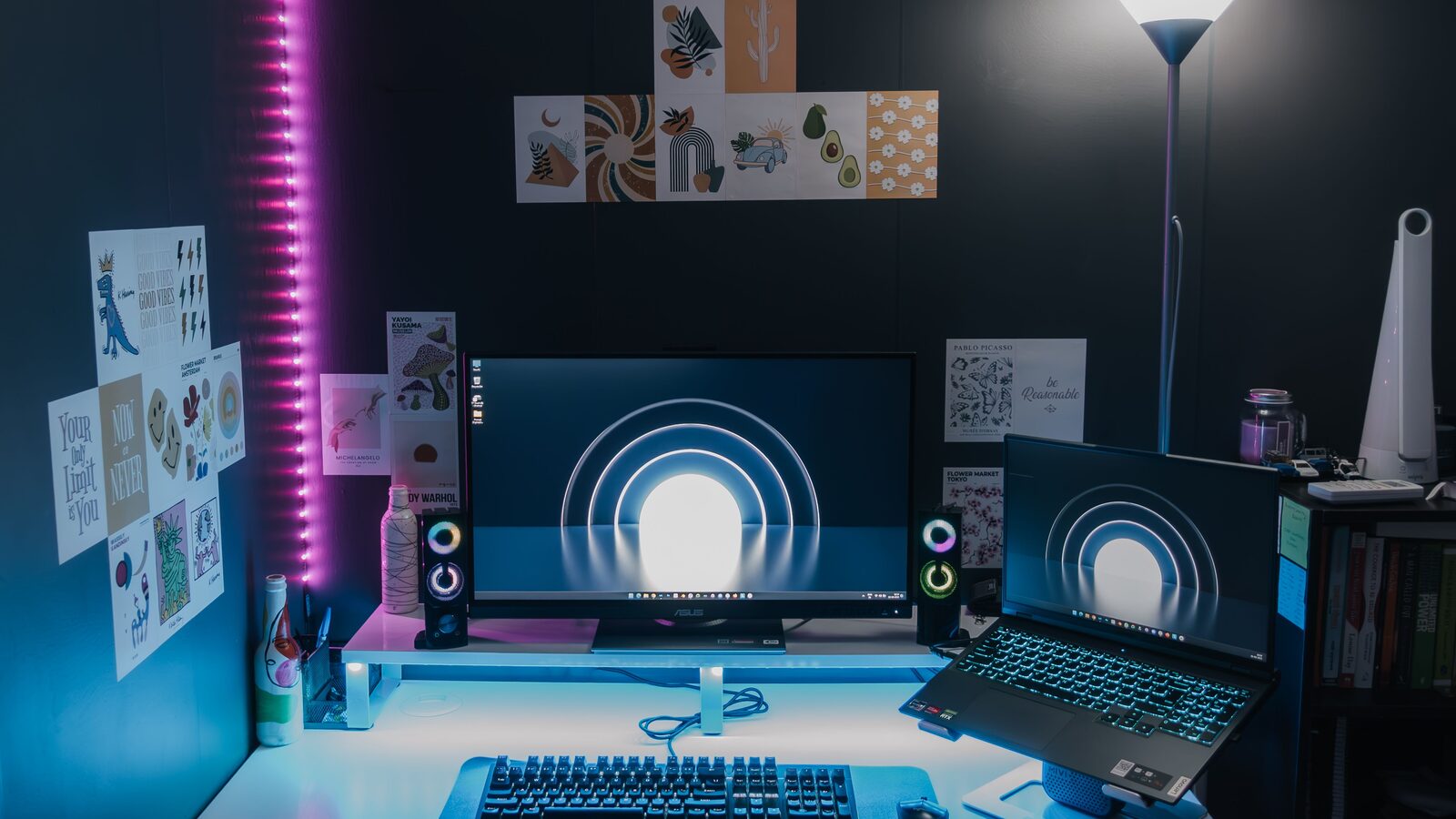 Configuração de jogos para PC com monitor, portátil, teclado e iluminação azul e rosa.