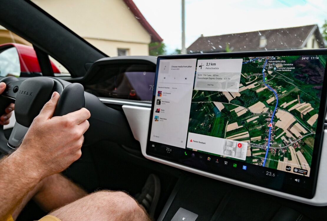 Condutor segura o volante de um Tesla enquanto o ecrã central mostra um percurso de navegação.