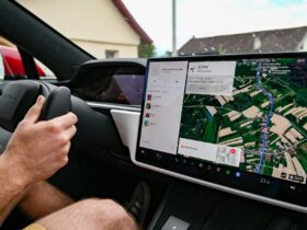 Condutor segura o volante de um Tesla enquanto o ecrã central mostra um percurso de navegação.