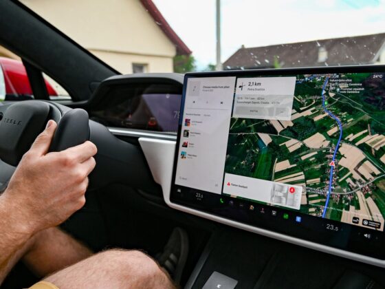 Condutor segura o volante de um Tesla enquanto o ecrã central mostra um percurso de navegação.