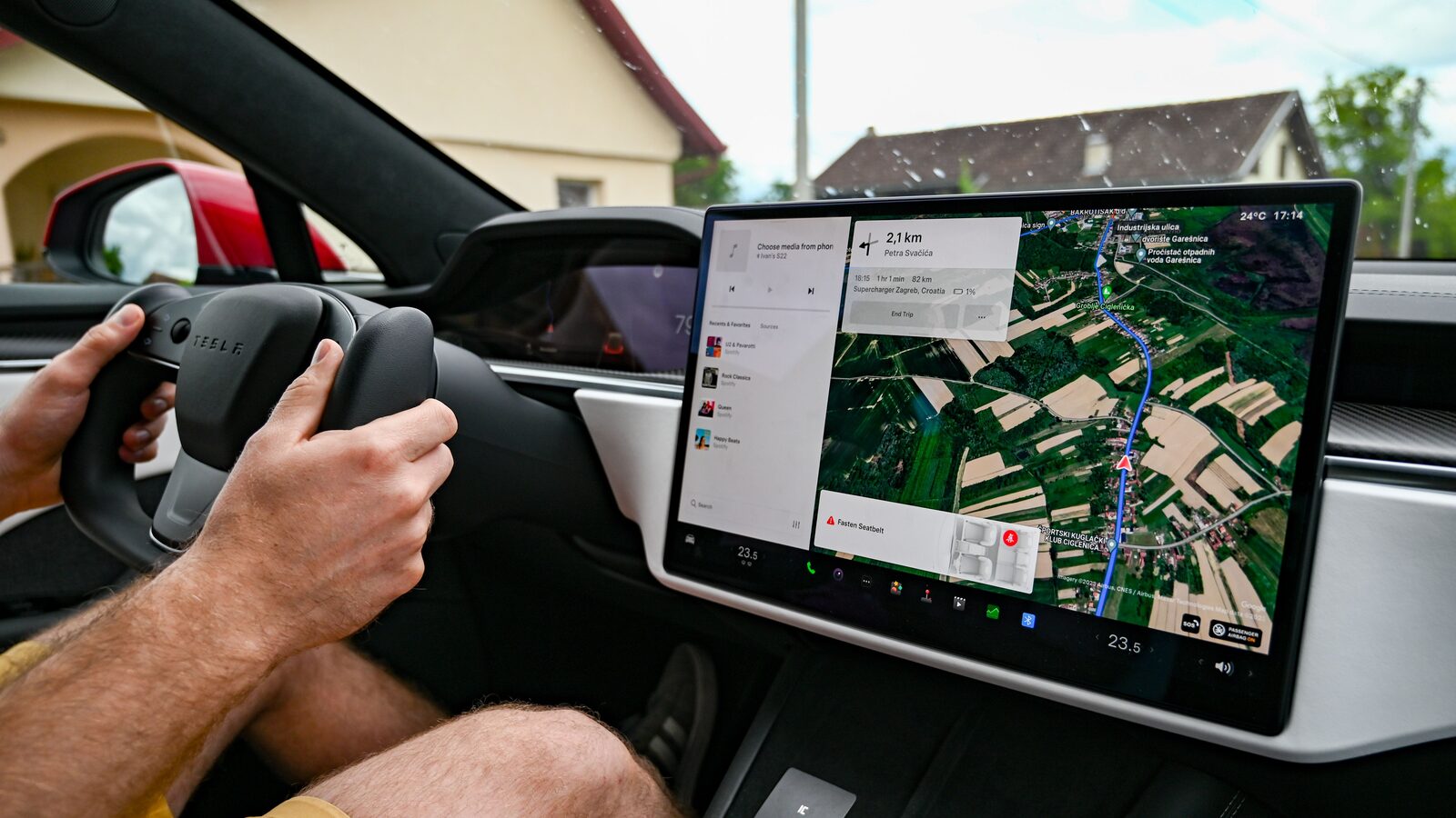 Condutor segura o volante de um Tesla enquanto o ecrã central mostra um percurso de navegação.