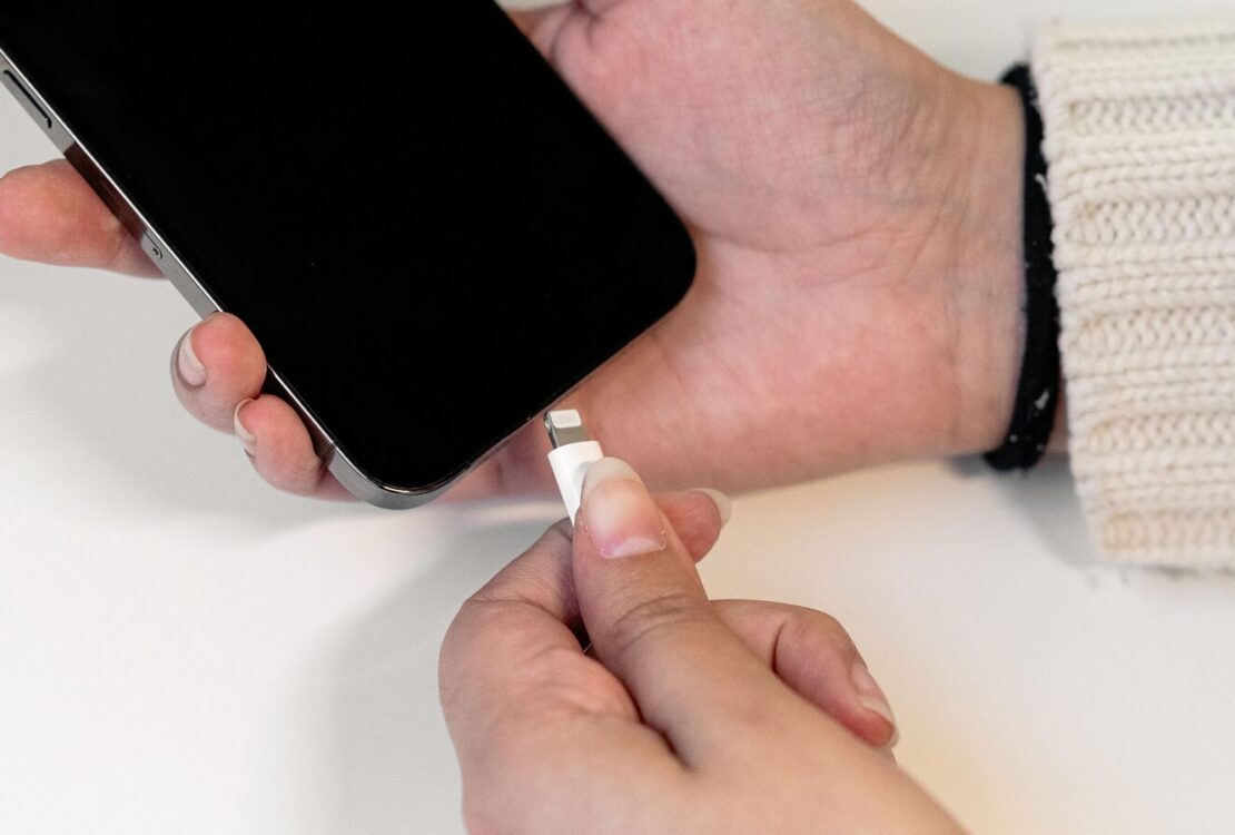 Mãos seguram um iPhone e aproximam um conector Lightning da porta do telemóvel.