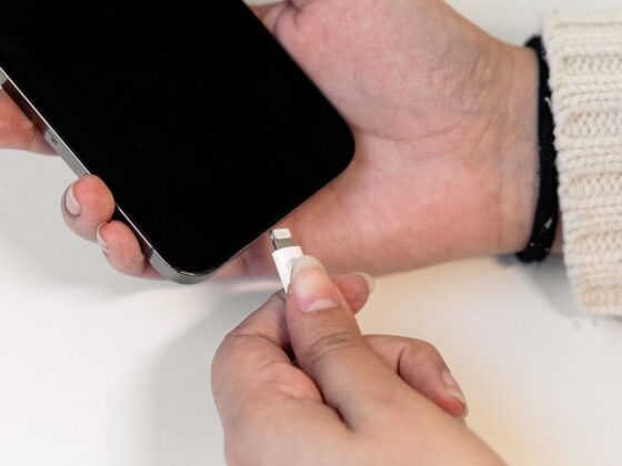 Mãos seguram um iPhone e aproximam um conector Lightning da porta do telemóvel.