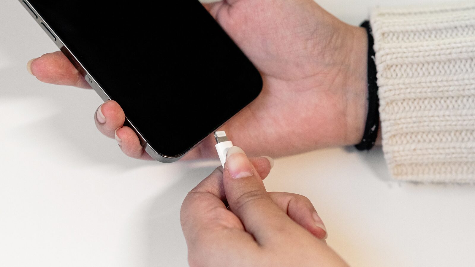 Mãos seguram um iPhone e aproximam um conector Lightning da porta do telemóvel.