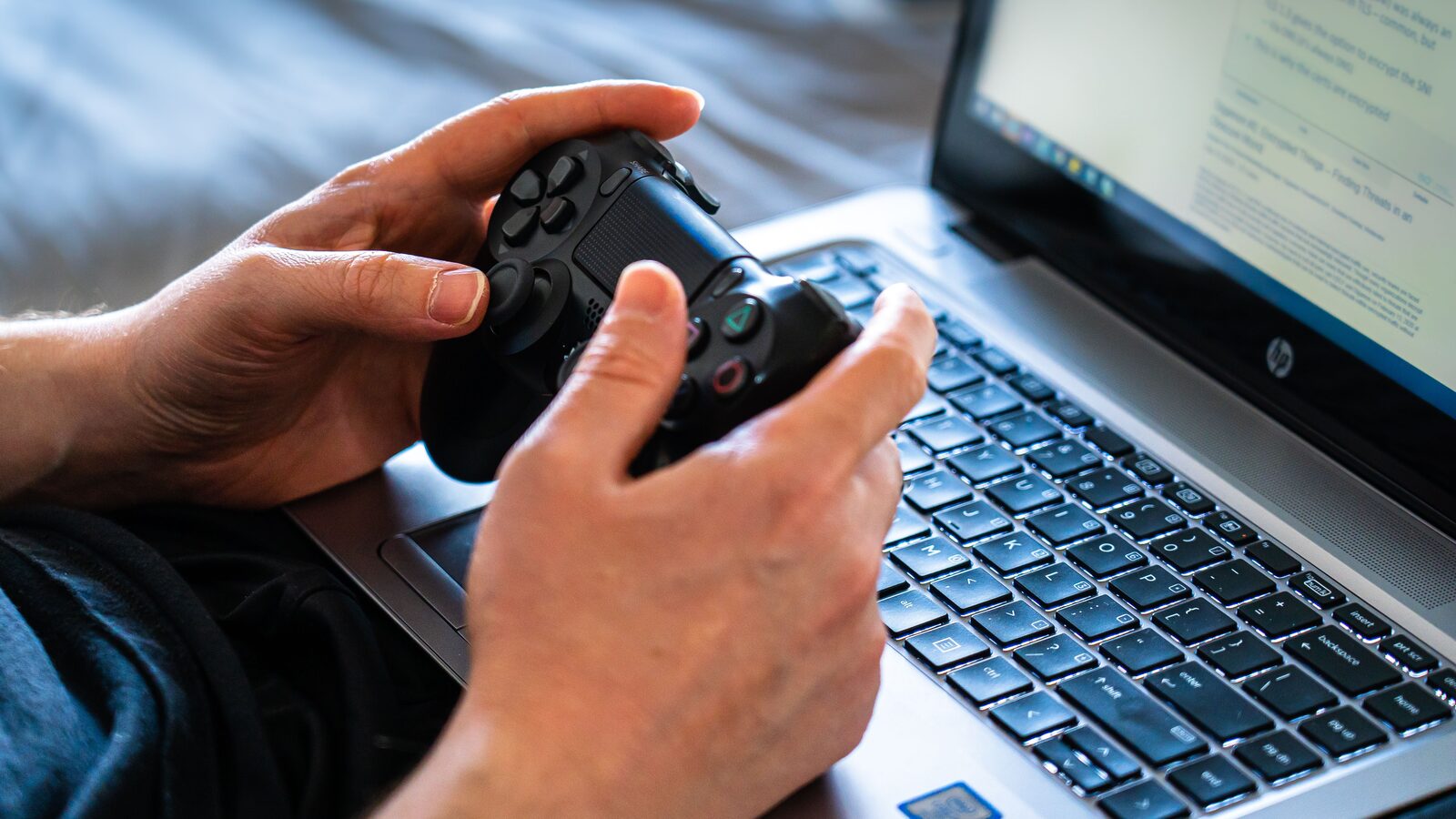Pessoa segura um controle de videogame diante de um laptop aberto sobre o teclado.