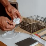 Pessoa segura um carregador branco junto a um portátil aberto numa secretária.