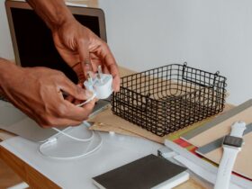 Pessoa segura um carregador branco junto a um portátil aberto numa secretária.