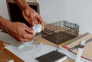 Pessoa segura um carregador branco junto a um portátil aberto numa secretária.