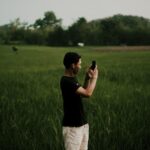 Homem usa um smartphone em um campo aberto cercado por vegetação.