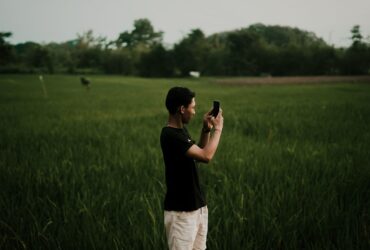 Homem usa um smartphone em um campo aberto cercado por vegetação.